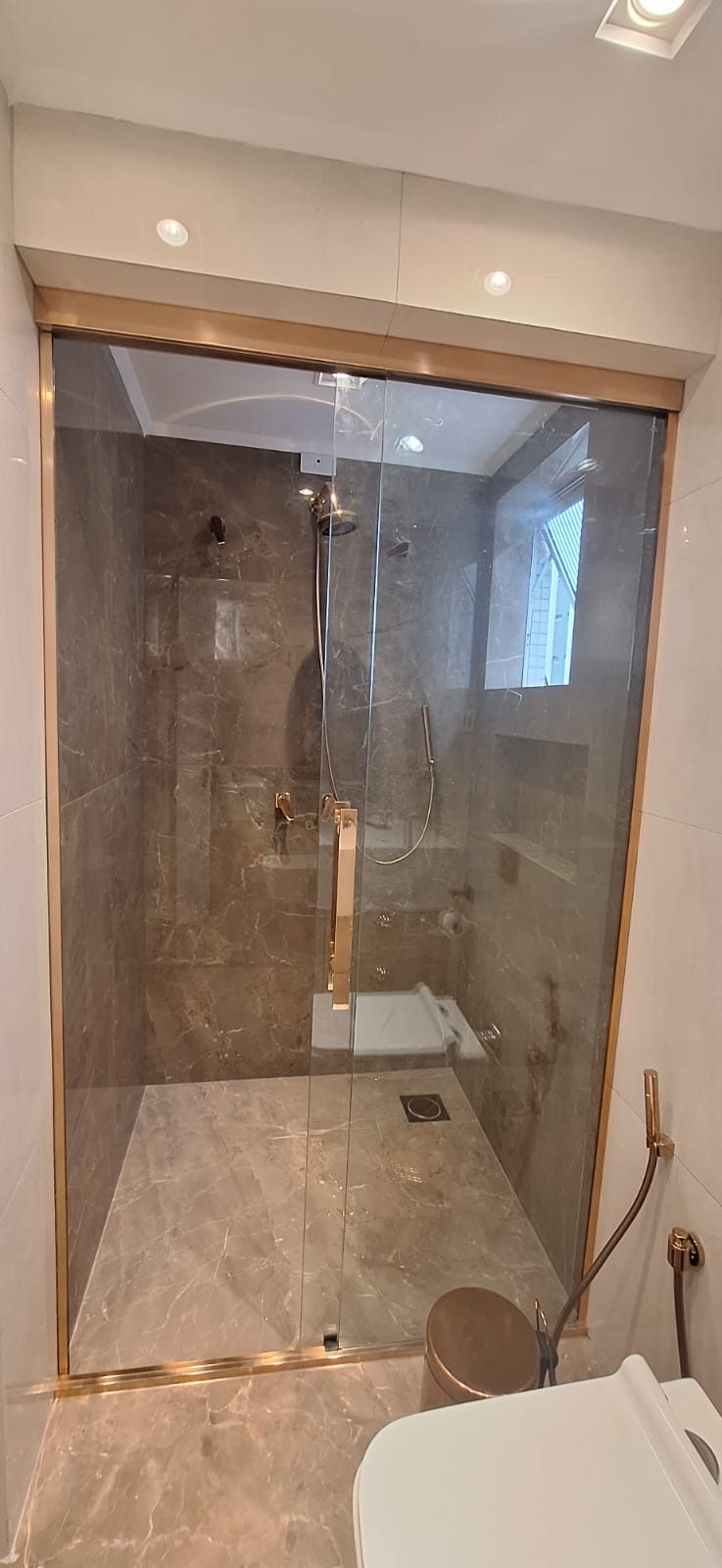Box de banho com perfil dourado e porcelanato marmorizado
